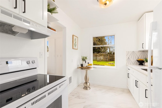 kitchen featuring white electric stove, marble finish floor, under cabinet range hood, white cabinetry, and backsplash