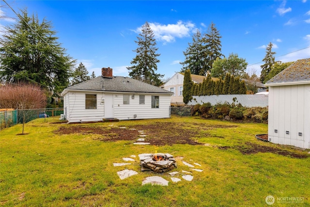 back of property featuring a yard, an outdoor fire pit, a chimney, and a fenced backyard