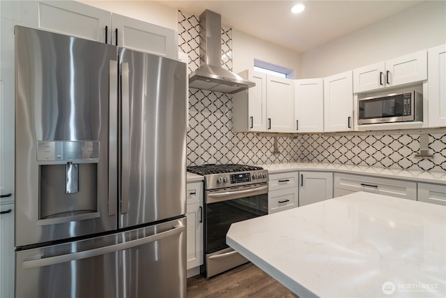 kitchen with wall chimney range hood, appliances with stainless steel finishes, light stone countertops, and white cabinets