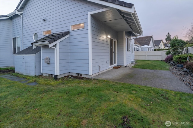 back house at dusk featuring a patio and a lawn