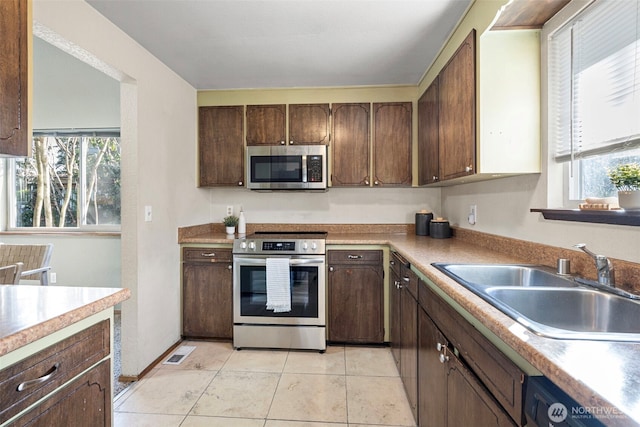 kitchen with light countertops, appliances with stainless steel finishes, a sink, and a wealth of natural light