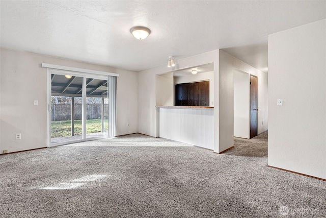 unfurnished living room with carpet floors, baseboards, and a textured ceiling