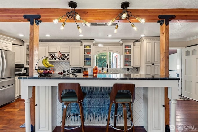 kitchen with stainless steel refrigerator, crown molding, a kitchen bar, and dark wood-type flooring