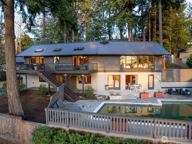 rear view of property featuring a patio, metal roof, stairs, an outdoor pool, and stucco siding