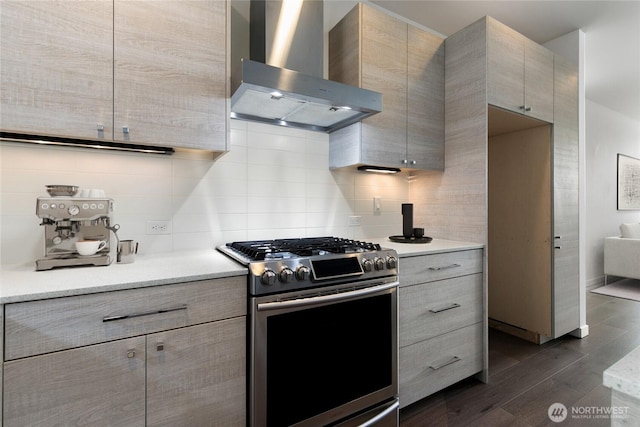 kitchen featuring light countertops, decorative backsplash, dark wood-type flooring, stainless steel gas stove, and wall chimney exhaust hood