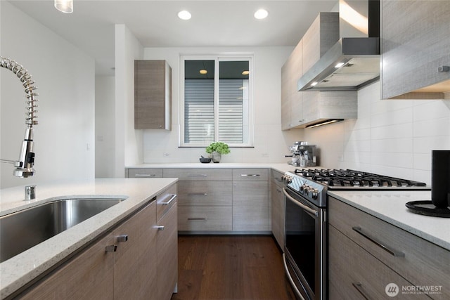 kitchen featuring light stone counters, dark wood-style floors, a sink, wall chimney range hood, and stainless steel gas range