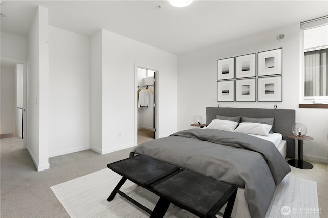 bedroom featuring baseboards, a walk in closet, and light colored carpet