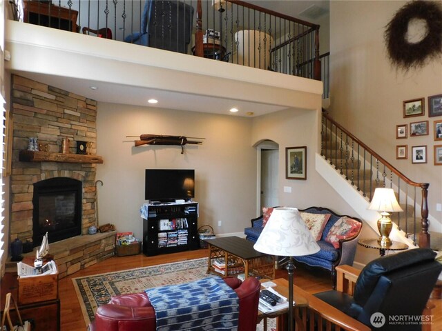 living room featuring a high ceiling, a fireplace, arched walkways, and wood finished floors