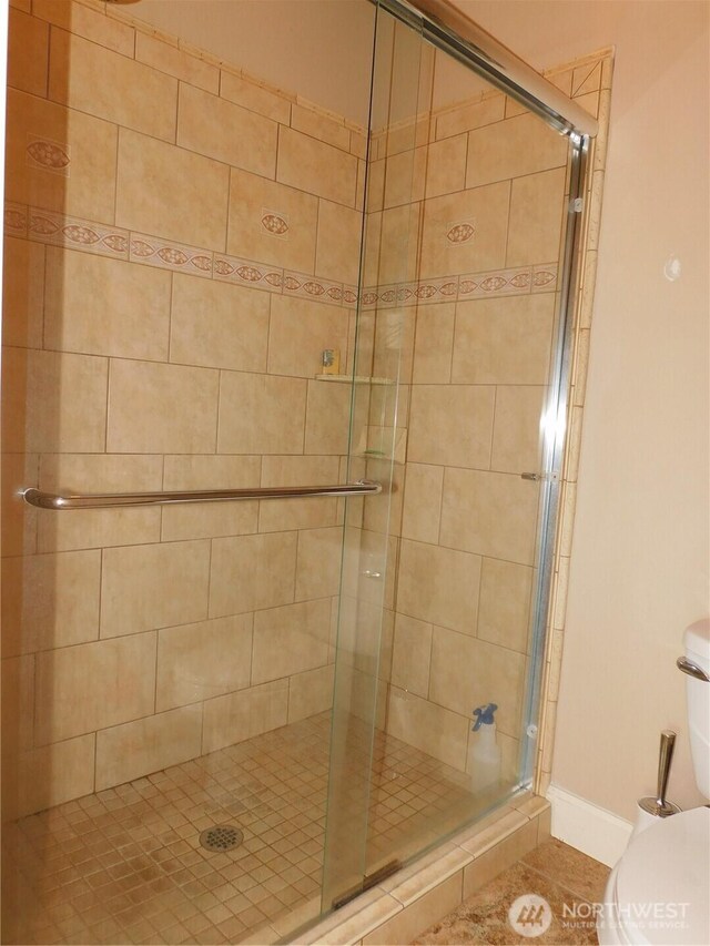 full bath with toilet, a stall shower, and baseboards