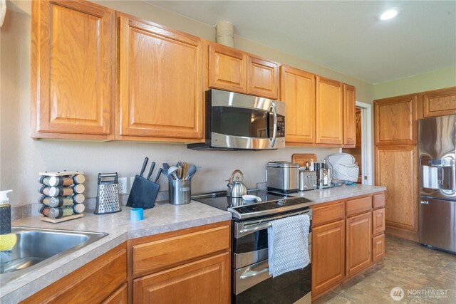 kitchen featuring stainless steel appliances, brown cabinetry, light countertops, and a sink