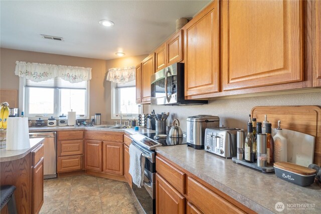 kitchen featuring stainless steel appliances, a sink, visible vents, light countertops, and brown cabinets