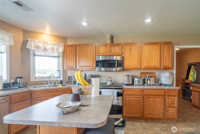 kitchen with a kitchen island, stainless steel appliances, a sink, and light countertops