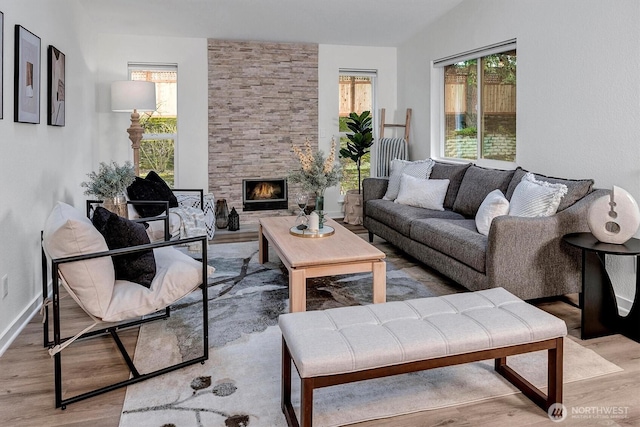 living room featuring vaulted ceiling, light wood-style floors, and a stone fireplace