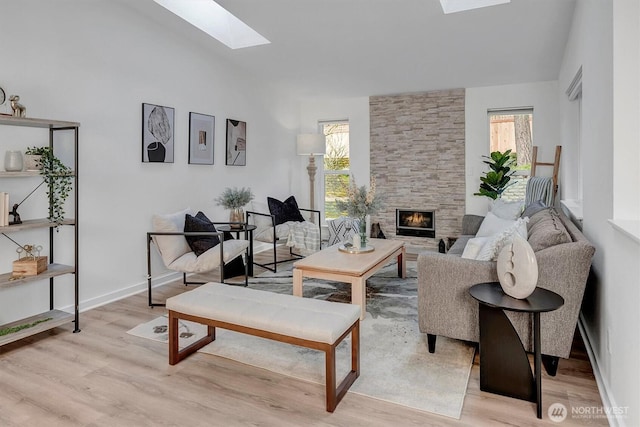 living room with a stone fireplace, light wood-type flooring, baseboards, and a skylight