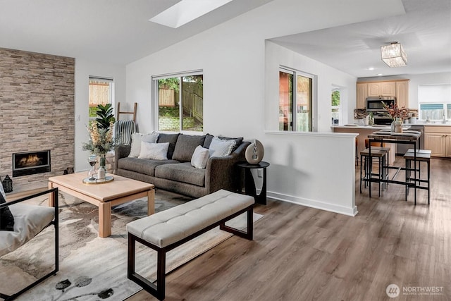 living area with plenty of natural light, vaulted ceiling with skylight, a fireplace, and wood finished floors