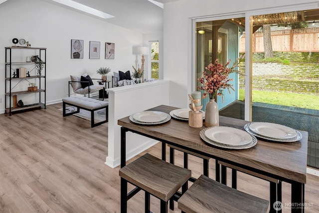 dining room with baseboards, light wood-style floors, and vaulted ceiling with skylight