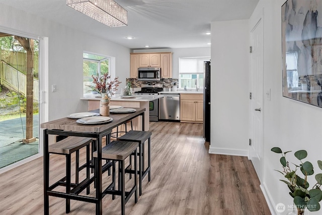 kitchen featuring light wood finished floors, light brown cabinets, tasteful backsplash, light countertops, and appliances with stainless steel finishes