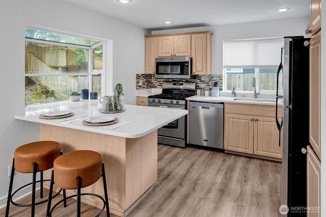 kitchen with a breakfast bar area, light countertops, stainless steel appliances, light brown cabinets, and a sink