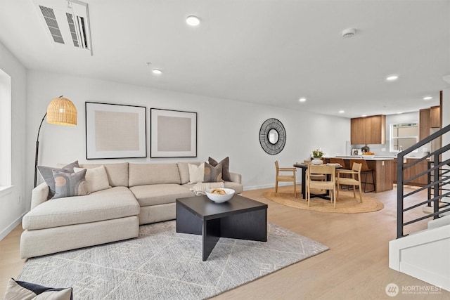 living room with recessed lighting, light wood-style flooring, stairs, and visible vents