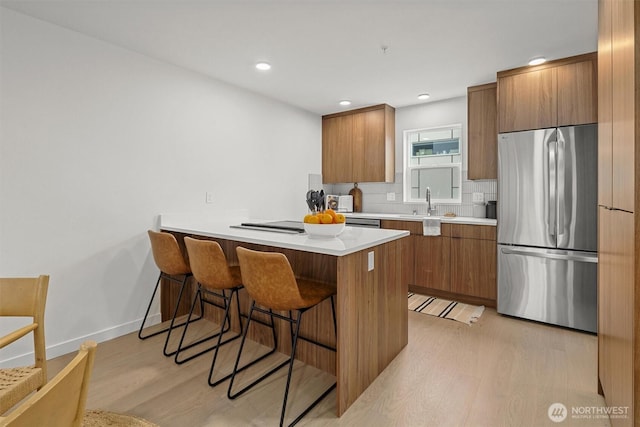 kitchen featuring light wood finished floors, brown cabinets, a kitchen breakfast bar, and freestanding refrigerator