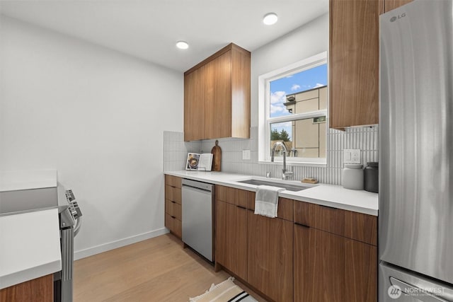 kitchen featuring light wood finished floors, a sink, tasteful backsplash, appliances with stainless steel finishes, and light countertops