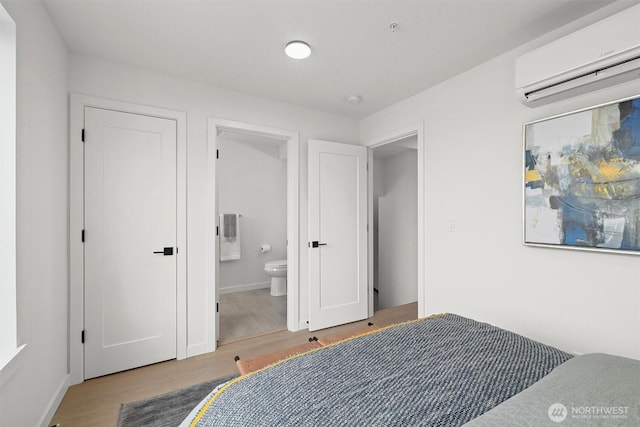 bedroom with a wall mounted air conditioner, baseboards, wood finished floors, and ensuite bathroom