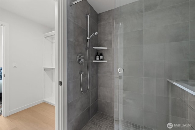 full bathroom featuring a stall shower, a walk in closet, baseboards, and wood finished floors