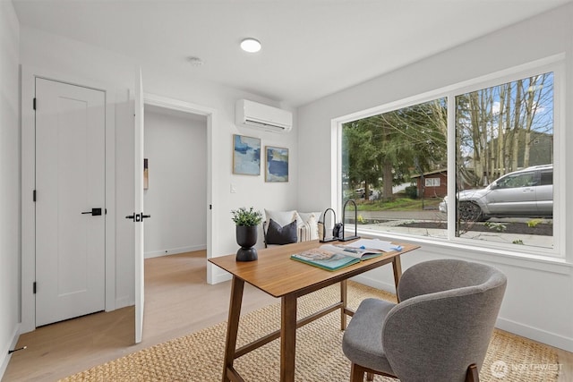 home office featuring a wall mounted air conditioner, baseboards, and light wood finished floors