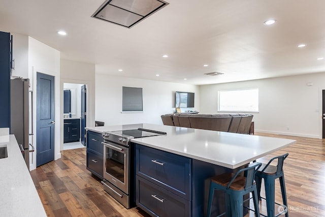 kitchen with blue cabinetry, stainless steel appliances, a kitchen island, dark wood-type flooring, and a kitchen breakfast bar