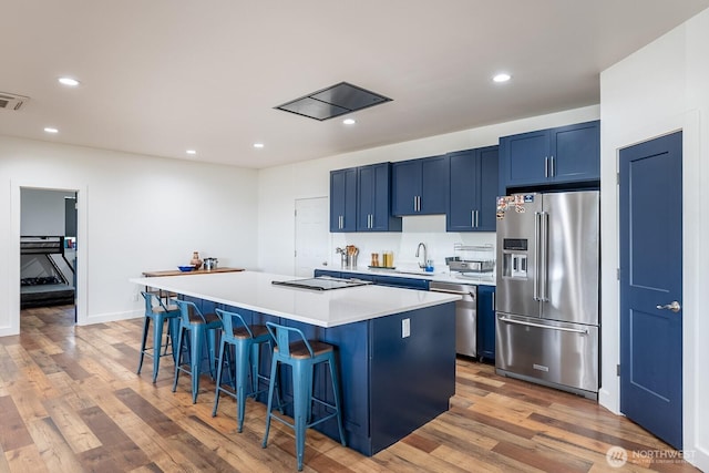 kitchen with stainless steel appliances, a kitchen island, light hardwood / wood-style floors, blue cabinets, and a kitchen bar