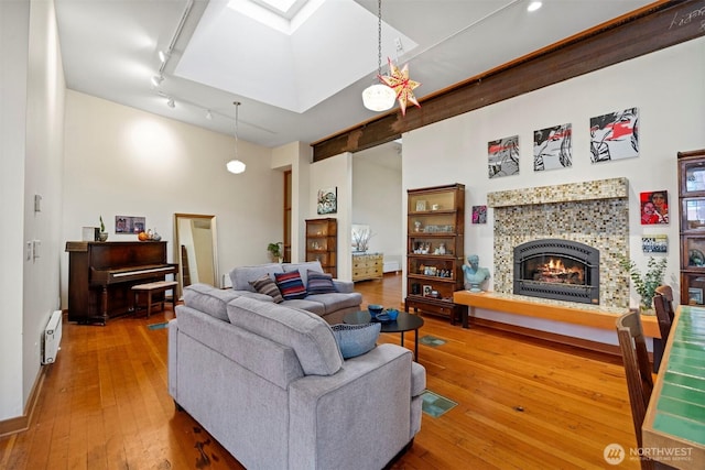 living area with a tile fireplace, a skylight, wood finished floors, visible vents, and baseboard heating