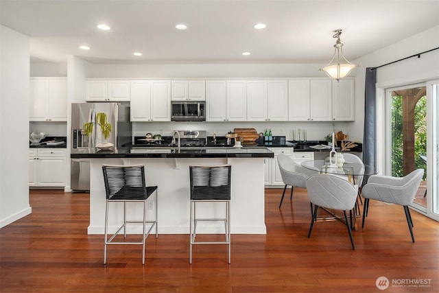 kitchen with appliances with stainless steel finishes, a breakfast bar, dark hardwood / wood-style flooring, white cabinets, and a kitchen island with sink