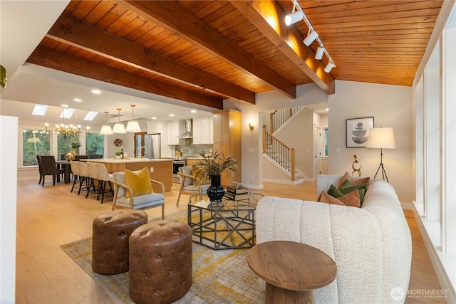 living room featuring beam ceiling, light wood-style flooring, stairway, wooden ceiling, and baseboards