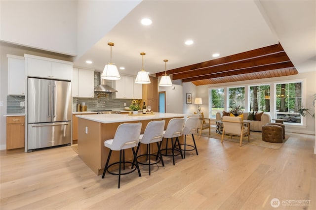 kitchen with white cabinets, light countertops, a center island with sink, freestanding refrigerator, and decorative light fixtures