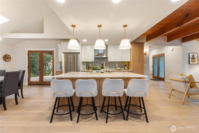 kitchen featuring high end refrigerator, white cabinets, french doors, an island with sink, and decorative light fixtures