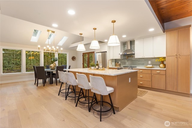 kitchen with white cabinets, a spacious island, wall chimney exhaust hood, lofted ceiling with skylight, and pendant lighting