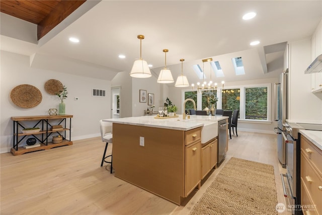 kitchen featuring decorative light fixtures, a center island with sink, stainless steel appliances, visible vents, and a sink