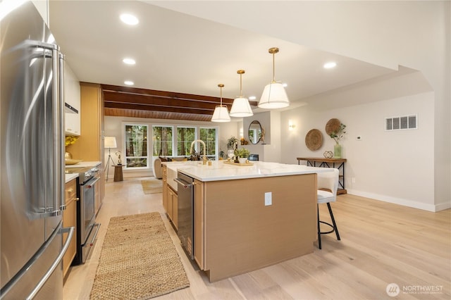 kitchen with visible vents, an island with sink, appliances with stainless steel finishes, decorative light fixtures, and a kitchen bar