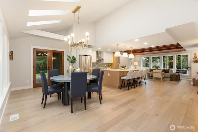 dining space with baseboards, visible vents, a chandelier, light wood-type flooring, and high vaulted ceiling