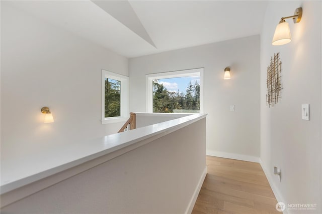 hallway with light wood-style floors, baseboards, and an upstairs landing