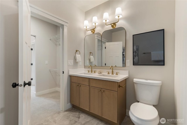 full bathroom with double vanity, baseboards, a walk in closet, and a sink