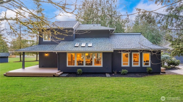 rear view of property with a wooden deck, a lawn, and roof with shingles