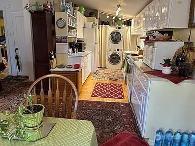 kitchen with white cabinetry, stacked washer / dryer, stainless steel refrigerator, and vaulted ceiling