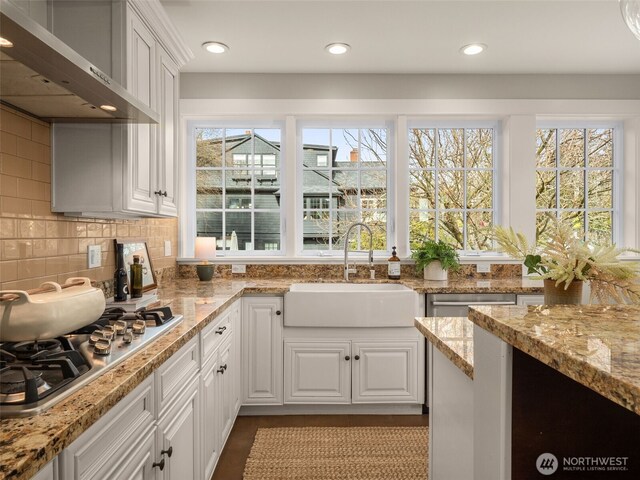 kitchen featuring stainless steel gas stovetop, white cabinets, a sink, light stone countertops, and wall chimney exhaust hood