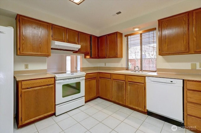 kitchen featuring white appliances, brown cabinetry, light countertops, under cabinet range hood, and a sink