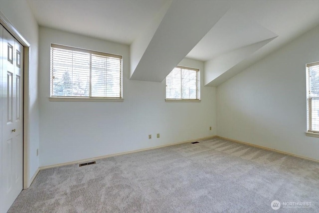 additional living space featuring light carpet, baseboards, visible vents, and lofted ceiling