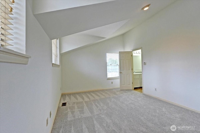 spare room with lofted ceiling, baseboards, visible vents, and light colored carpet