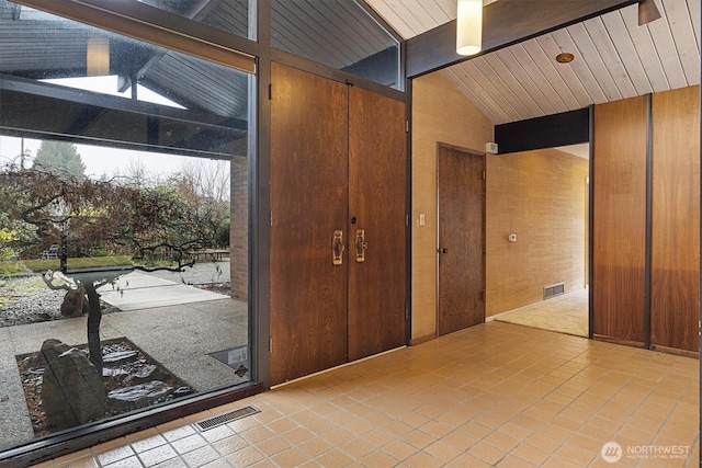 interior space featuring lofted ceiling with beams, light tile patterned floors, wooden walls, and visible vents