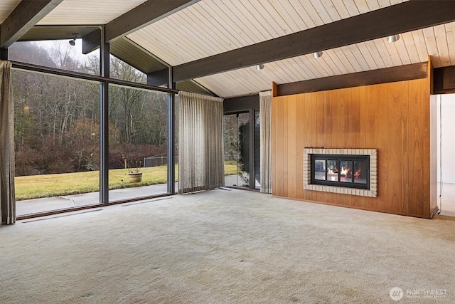 unfurnished living room featuring carpet floors, vaulted ceiling with beams, a brick fireplace, wood walls, and a wall of windows