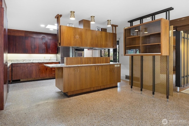 kitchen featuring glass insert cabinets, freestanding refrigerator, a center island, light countertops, and light speckled floor